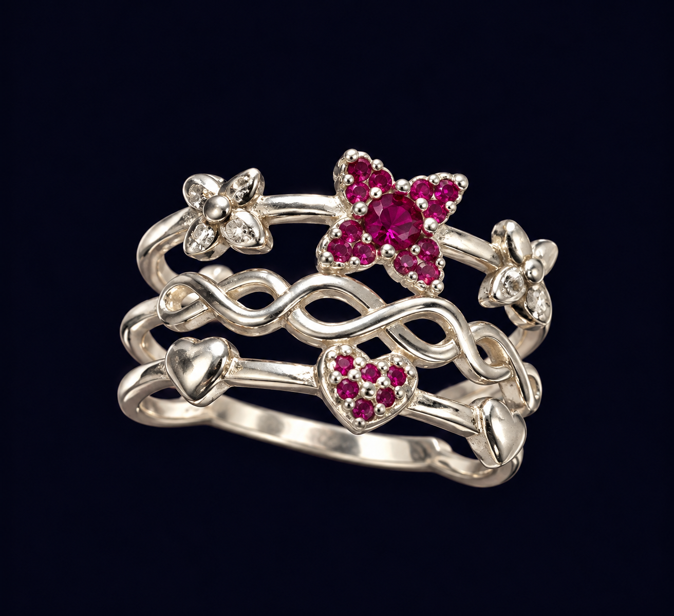 Composição de anéis com flores, motivos de infinito e corações, com detalhes em rosa intenso sobre fundo escuro.