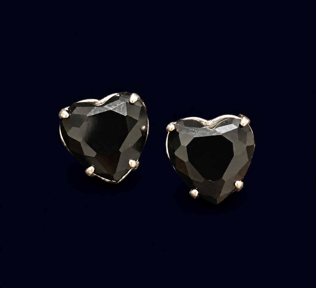 Par de brincos em formato de coração preto facetado com garras aparentes.