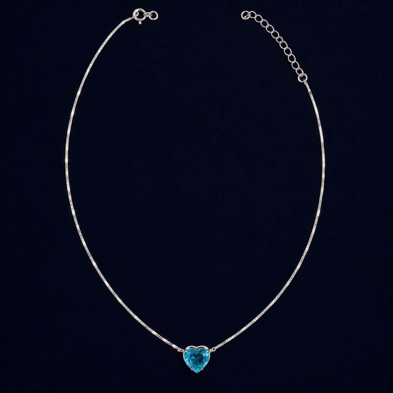 Colar de corrente fina com pingente azul em formato de coração sobre fundo escuro.