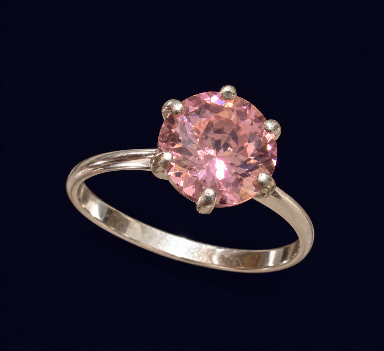 Anel com centro redondo rosa facetado, garras aparentes e aro liso.
