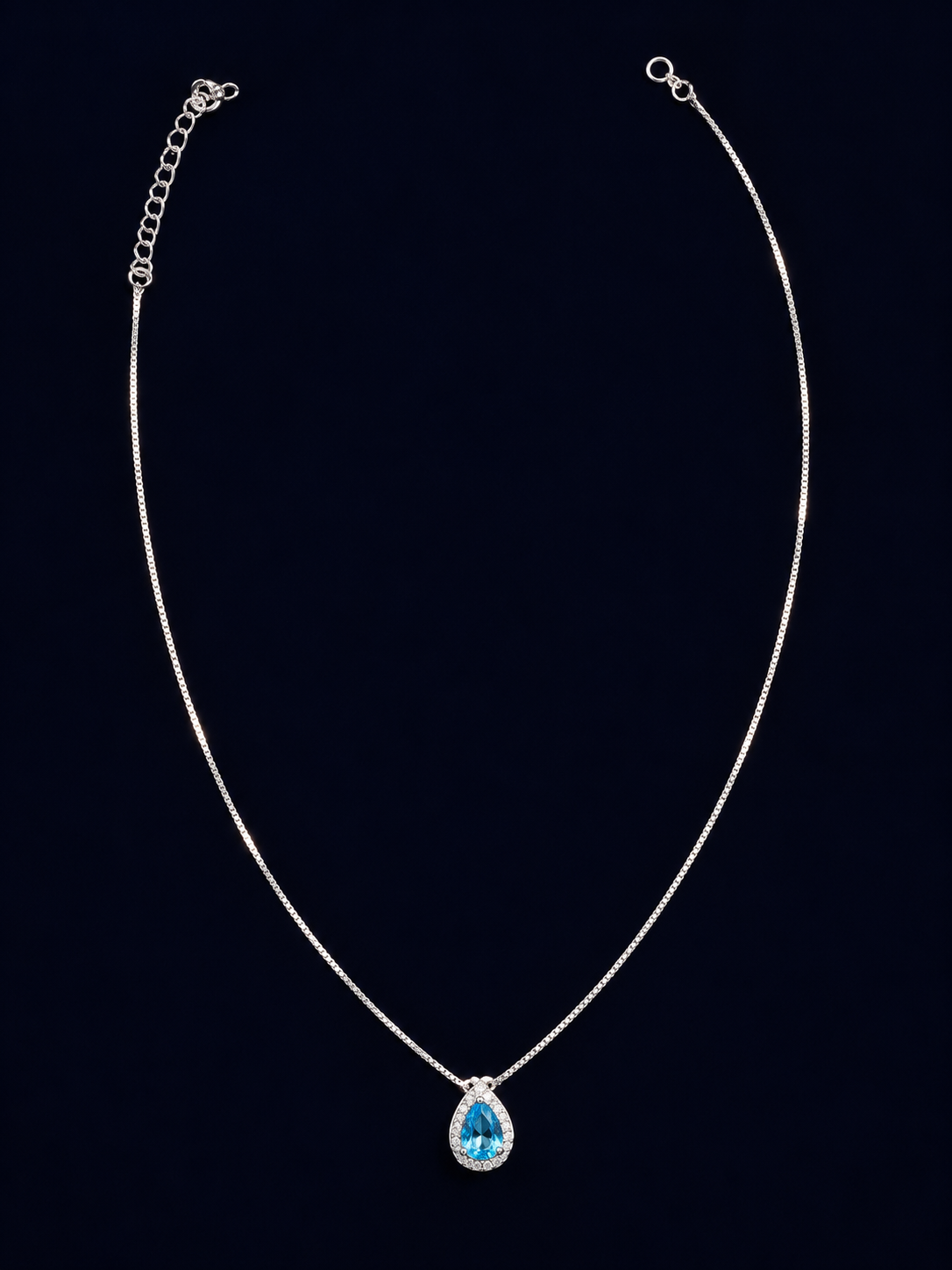 Colar de corrente fina com pingente em gota azul e contorno brilhante sobre fundo escuro.