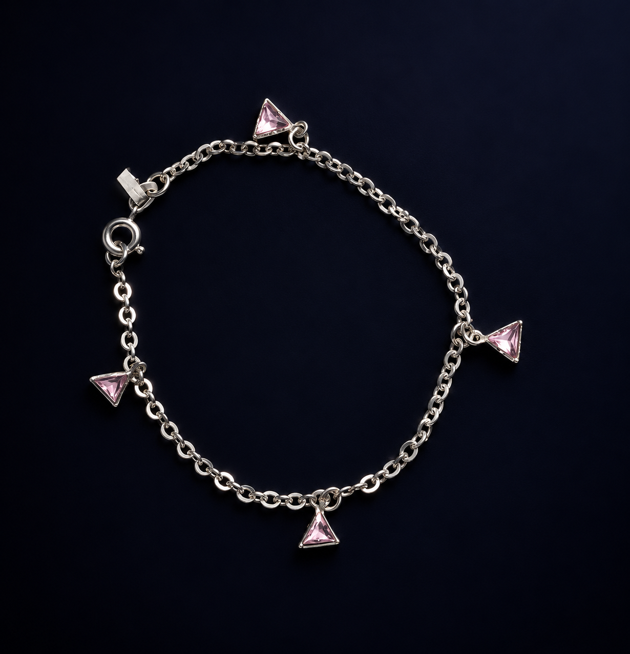 Pulseira de elos com quatro pingentes triangulares rosados sobre fundo escuro.
